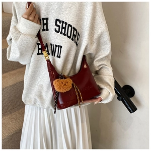Detail of burgundy leather shoulder bag with logo embossing and cute bear pendant