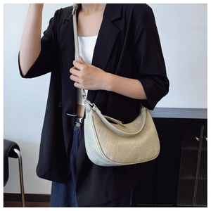 On-body view of a beige crescent hobo bag featuring a natural pleated leather texture