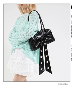 Detail of black glossy handbag featuring oversized bow and silver metal rivets
