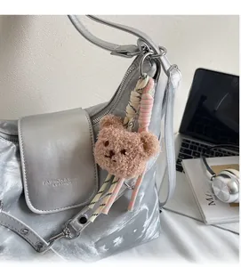 Detail der silbernen Metallic-Schultertasche mit Logo-Prägung und Plüschbär-Anhänger