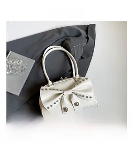 Detail of white leather bow handbag with silver metal studs and thin shoulder straps