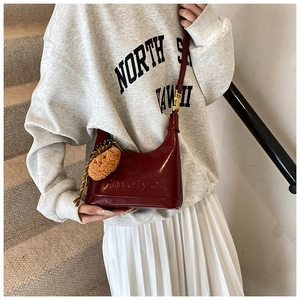 Detail of dark red glossy shoulder bag featuring embossed text and cute bear charm