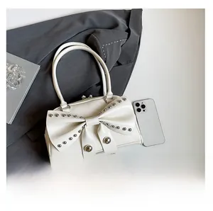 Detailed view of white chic handbag with oversized bow, metal studs, and glossy finish