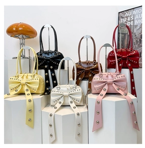 Bow handbag with rivets in multiple colors displayed on white geometric stands