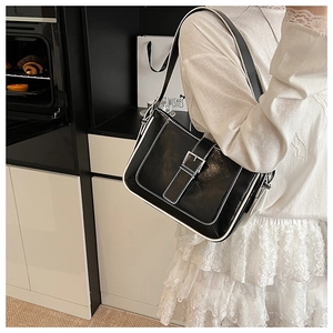 Close-up of black leather crescent shoulder bag with white stitching and silver buckle