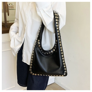 Détail d'un sac cabas en cuir noir clouté d'argent porté par un mannequin en chemise