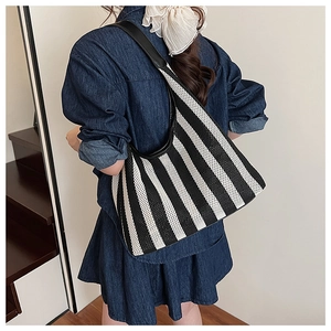 Detail of nautical striped knit tote bag with black leather strap on a model shoulder