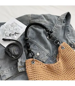 Close-up of woven tote bag featuring beaded handles and detachable black leather shoulder strap