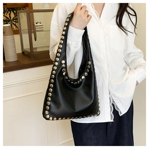 Detail of silver rivets on black leather hobo bag worn by model in a café