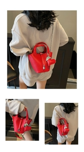 Detail of red lychee leather bucket bag with metal padlock and heart-shaped charm