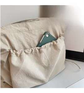 Detail of beige pleated tote bag showing large exterior pocket with a smartphone inside