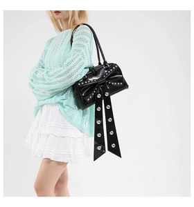 Close-up of black glossy bow handbag with silver studs and decorative long ribbons