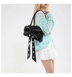 Detail of black shoulder bag with large bow and silver studs on a stylish model