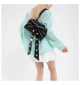 Détail du sac à nœud noir avec rivets porté avec un pull bleu et une jupe plissée blanche