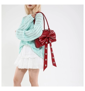 Detail of red patent leather handbag featuring oversized bow and silver metal rivets