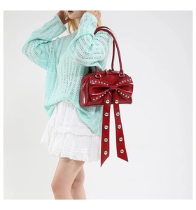 Détail du sac en cuir verni rouge foncé avec nœud géant et rivets porté par un mannequin