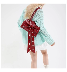 Détail du sac bandoulière rouge foncé avec nœud géant et rivets porté par un mannequin