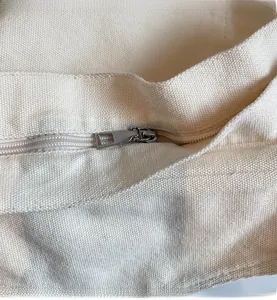 Detailed macro view of the smooth silver metal zipper on an off-white canvas crossbody bag