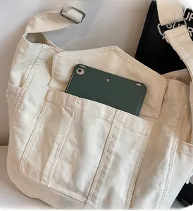 Detail of off-white canvas crossbody bag showing spacious front pockets and a tablet inside