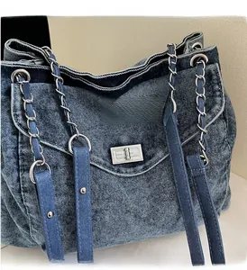 Detail of blue washed denim shoulder bag featuring silver metal turn-lock and chain strap
