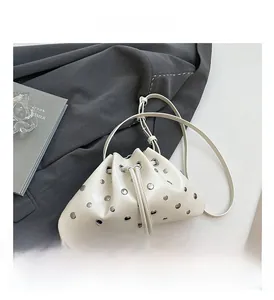 Detail view of cream dumpling bag featuring silver stud rivets and a thin leather strap
