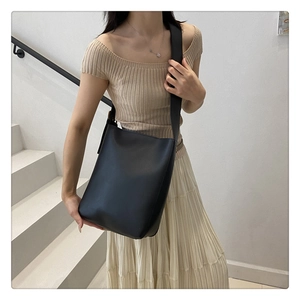 Close-up of a black minimalist matte leather bucket bag with a wide shoulder strap
