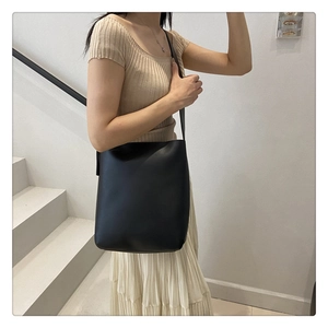 Minimalist black leather bucket bag shown on a model in a modern indoor staircase setting