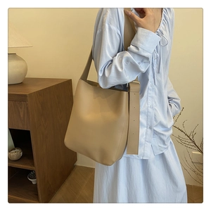 Detail of khaki leather bucket bag with wide strap and gold buckle on a model