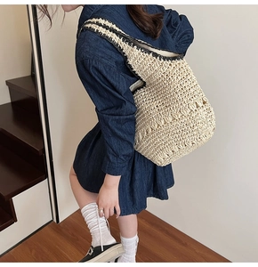 Detail of hand-woven straw tote bag with black crochet trim on a model shoulder