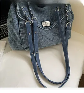 Detail of blue denim tote bag with silver chain strap and metal lock on desk