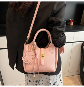 Detail of pink lychee leather bucket bag featuring a gold twist lock and a cute dog charm