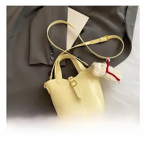 Detail van de crème lederen bucket bag met pluchen beer hanger op een grijze blazer