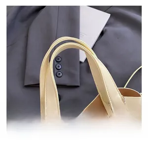 Detail van de crème handtas met gouden ritssluiting en een rode ruitvormige bedel