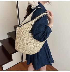 Model wearing a large woven straw bucket bag with black trim and contrast straps