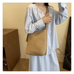 Minimalist khaki leather bucket bag with wide shoulder strap shown on a model