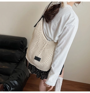 Detail of hand-woven hollow straw shoulder bag with black leather strap and logo patch