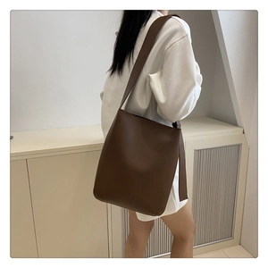 Detailed view of a dark brown bucket bag featuring minimalist leather and wide shoulder strap
