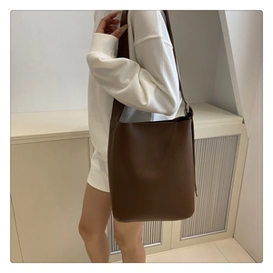 Detail of minimalist brown leather bucket bag with wide shoulder strap for daily commuting