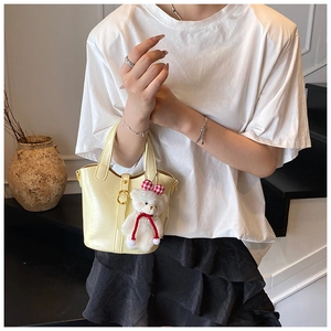 Chic cream leather bucket bag with cute plush bear pendant shown in a lifestyle setting