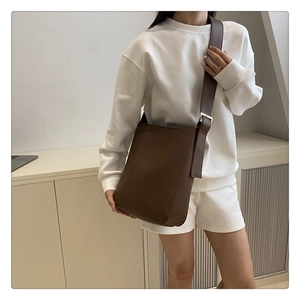 Detail of dark brown bucket bag with matte texture and silver adjustable buckle on wide strap