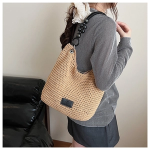 Detail of woven crossbody bag featuring black beaded strap and premium leather brand logo patch