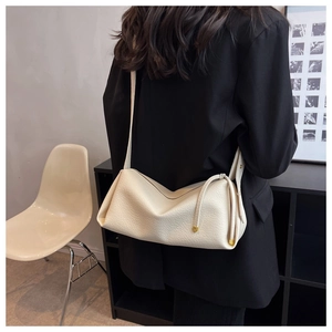 Close-up of off-white lychee grain leather pillow bag worn with black blazer