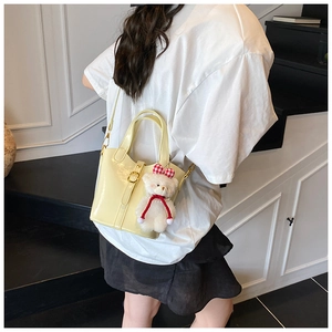 Sac seau jaune clair brillant avec porte-clés ours en peluche dans un décor d'escalier