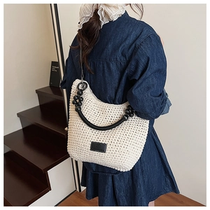 Detail of a beige hand-woven crochet shoulder bag with black handles and bead accents