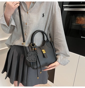 Detail of black lychee grain bucket bag with gold twist lock and dog charm in a lifestyle setting