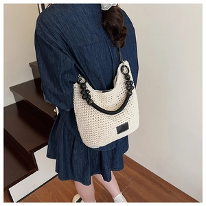 Detail of woven bucket bag featuring black bead accents and leather logo on beige knit