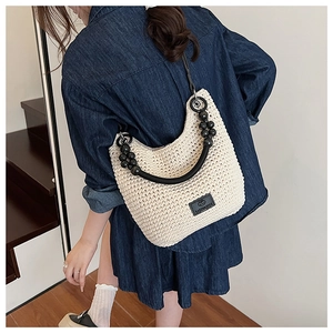 Detail of woven straw bucket bag with black bead handle and brand leather tag