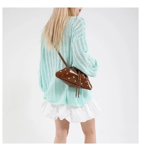 Close-up of brown patent leather bucket bag with silver rivets on model in casual outfit