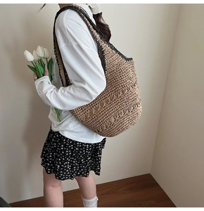 Large khaki straw tote bag with black woven trim shown on model for beach vacations