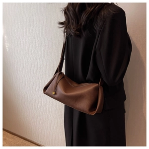 Detailed close-up of brown pebbled leather texture and metal charm on a crossbody bag